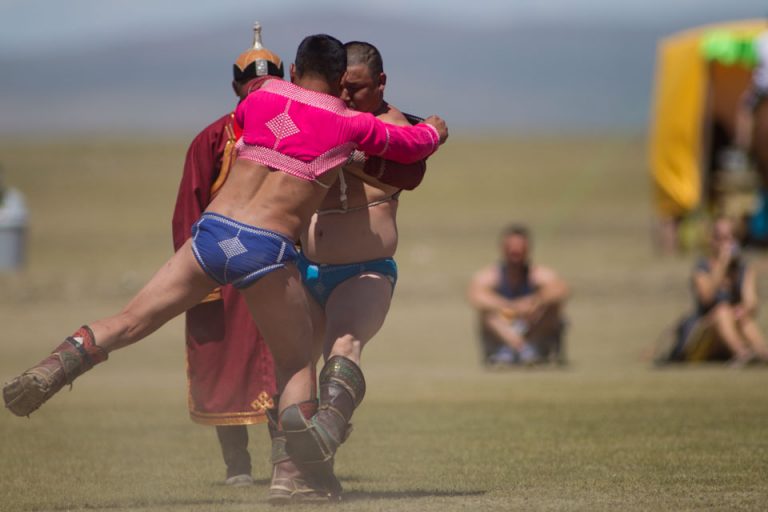 Two wrestlers battling it out at the Kharkhorin Naadam. Standing behind keeping an eye on the match is a 'zasuul' or judge.